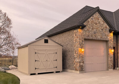 Tan a-frame style storage shed beside a house with stone accent