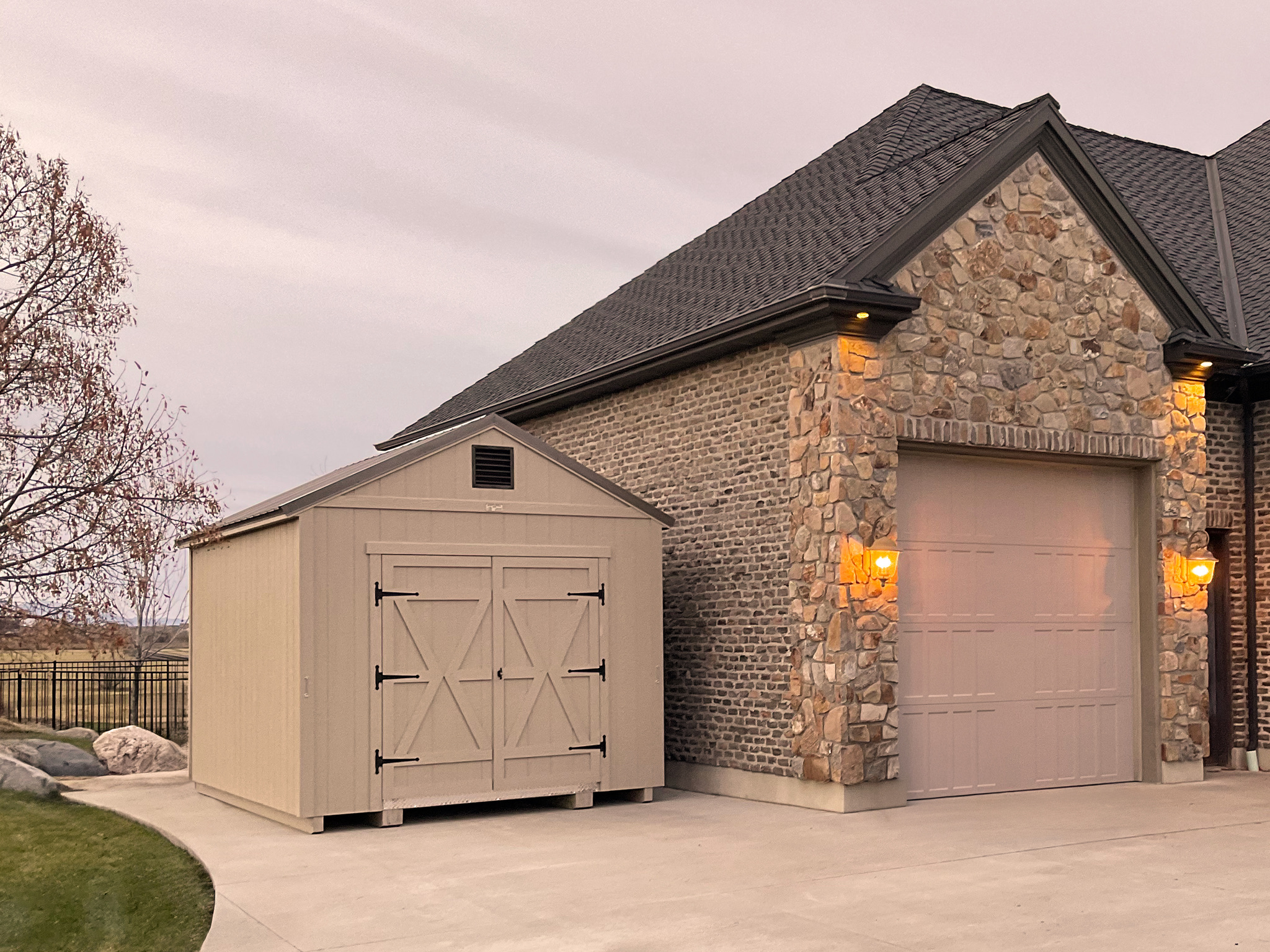 Tan a-frame style storage shed beside a house with stone accent