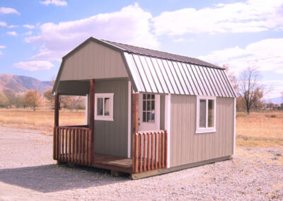 Tan barn style storage shed with a metal roof and wooden porch rails
