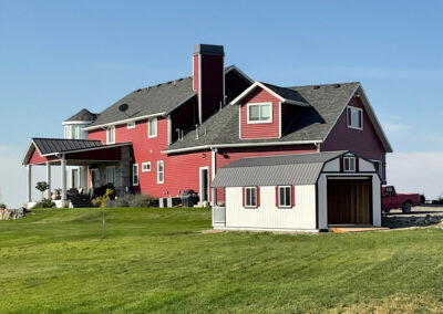 Barn style shed with an open garage door in front of a red house