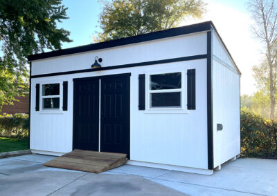 A white lean-to shed with black trim, double doors, and windows
